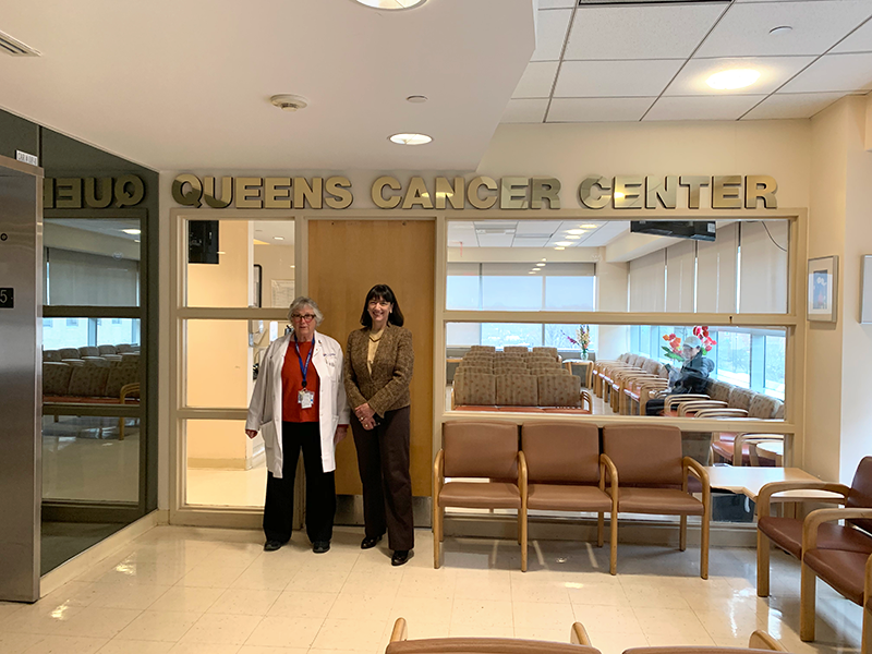 2 doctors stand together in a waiting room under a sign that says Queens Cancer Center