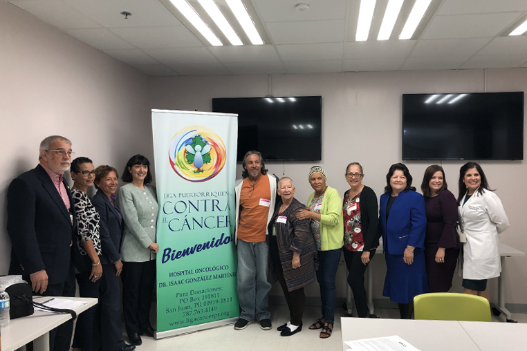 Photo of community members standing around a sign that says contra cáncer and bienvenido